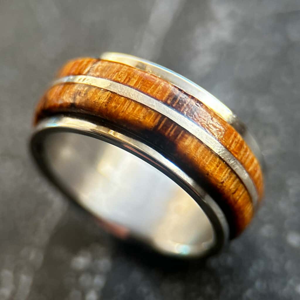 Marblewood fidget ring with silver inlay and silver edges on a neutral surface.