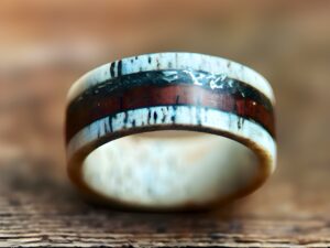 Deer antler wedding ring with tank scrap and rosewood inlay on wood table.