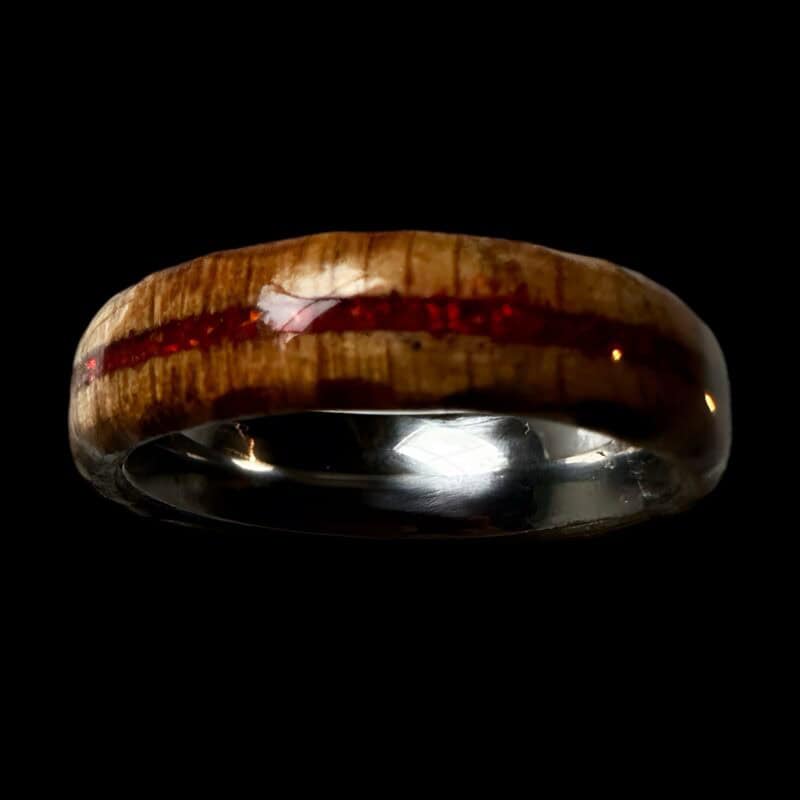 Ambrosia maple ring with red opal inlay, burnt edges, and stainless steel core. Set on black background.