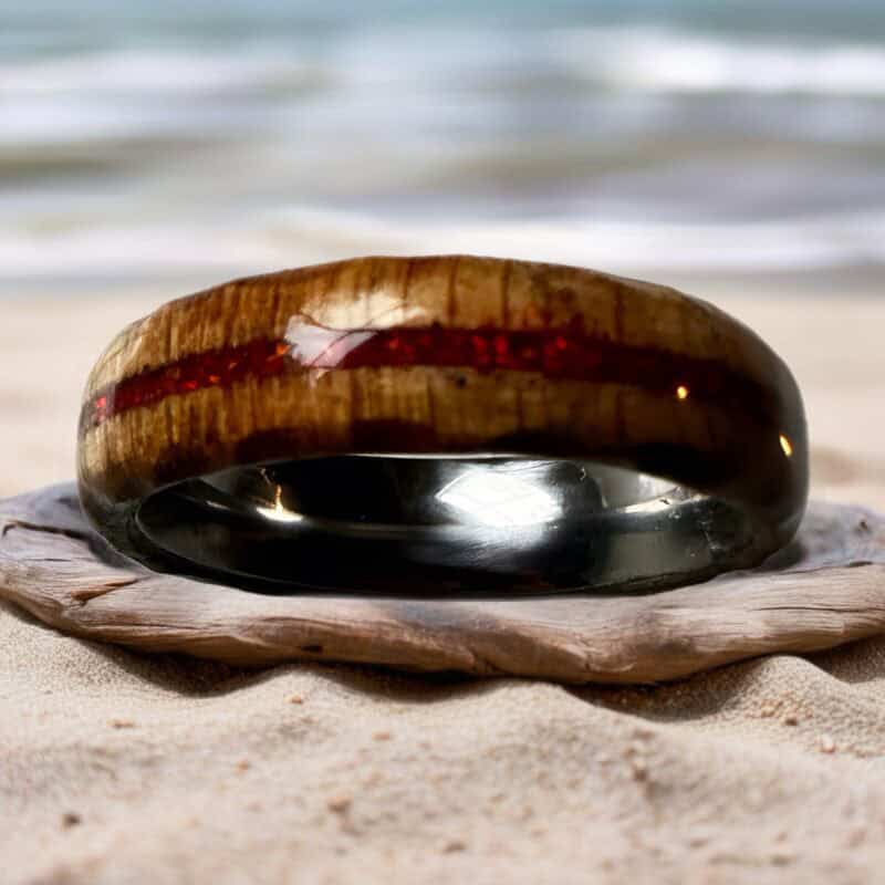 Ambrosia maple ring with red opal inlay, burnt edges, and stainless steel core. shown on beach