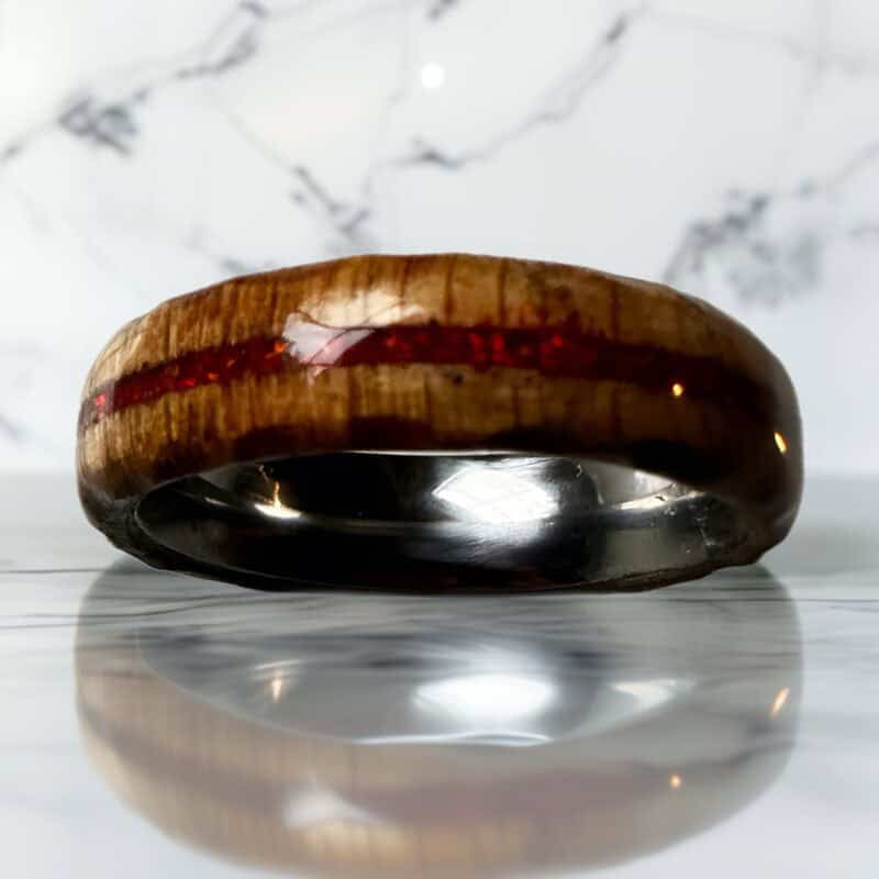 Ambrosia maple ring with red opal inlay, burnt edges, and stainless steel core. On a marble top.