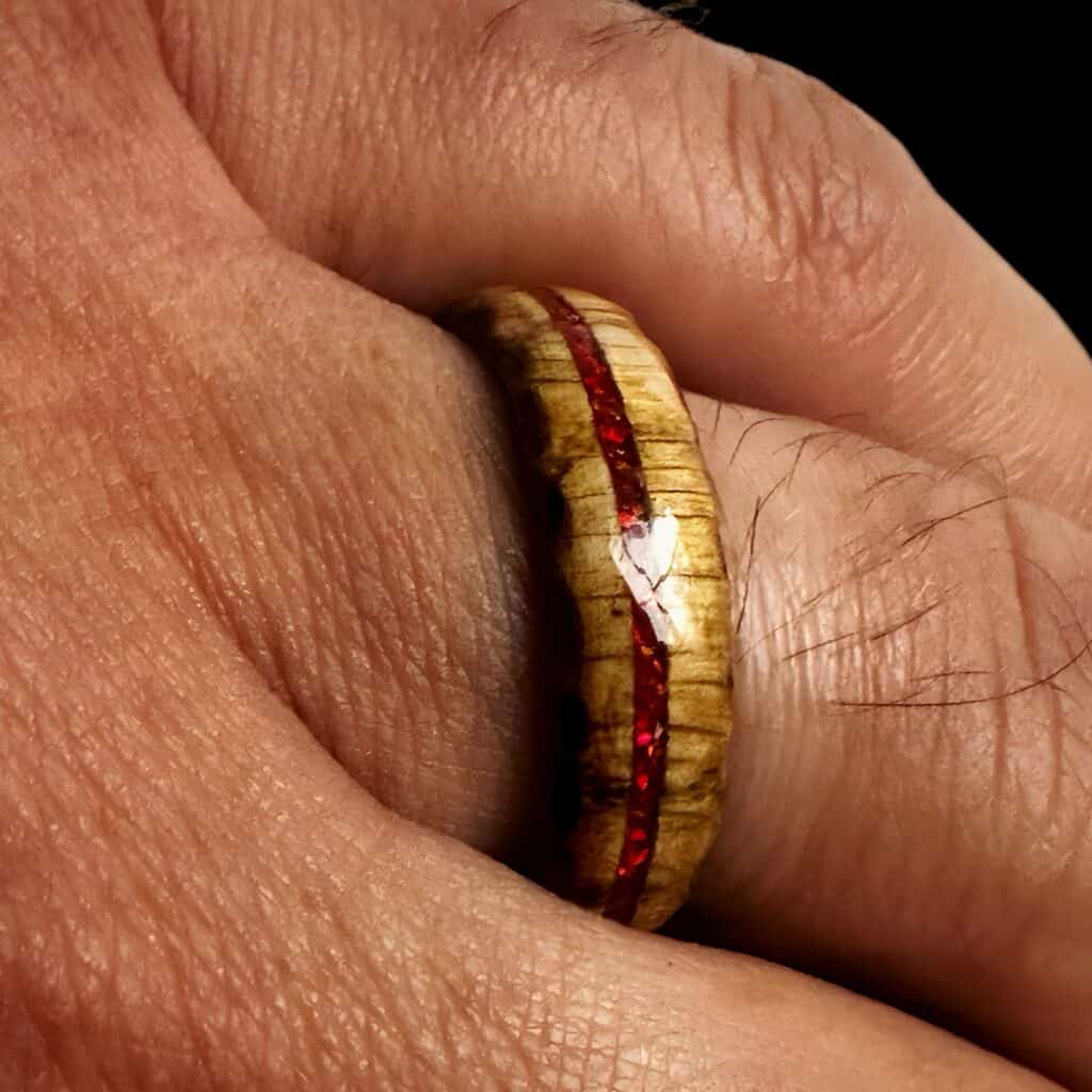 Ambrosia maple ring with red opal inlay, burnt edges, and stainless steel core. Shown on finger