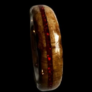 Ambrosia maple ring with red opal inlay, burnt edges, and stainless steel core. Set on black background.