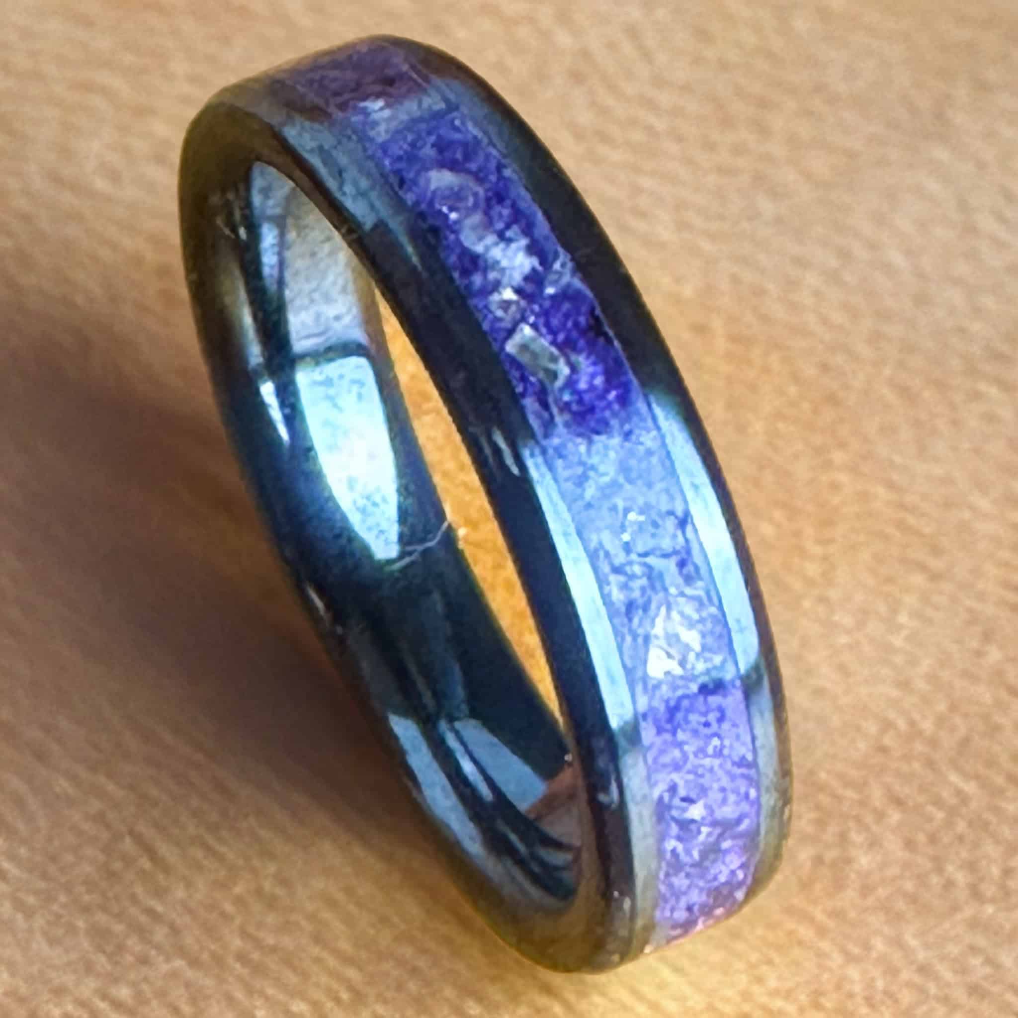 Purple glass ring. Black ceramic core. Set on a leather background,