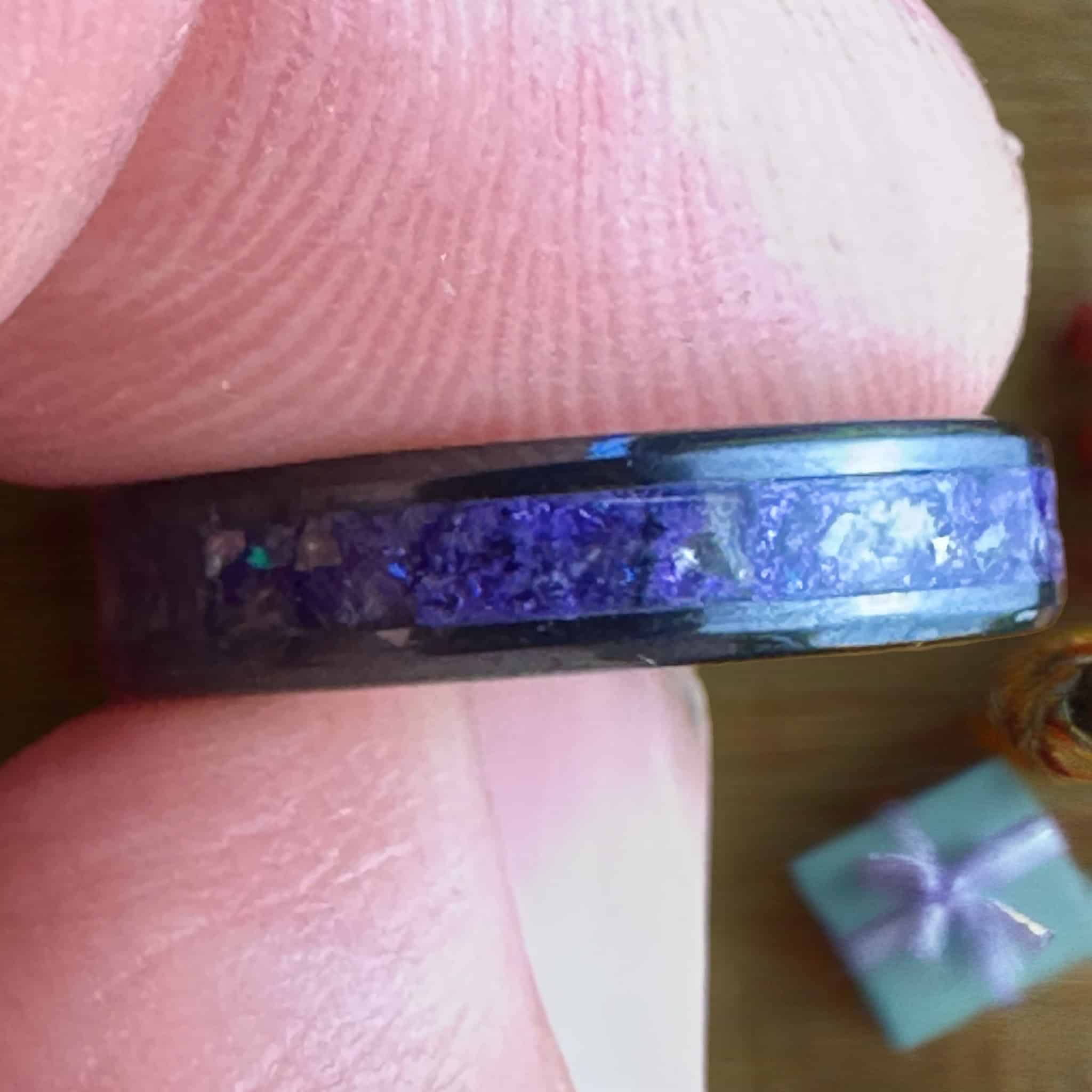 Purple glass ring. Black ceramic core. Held above a gift box.